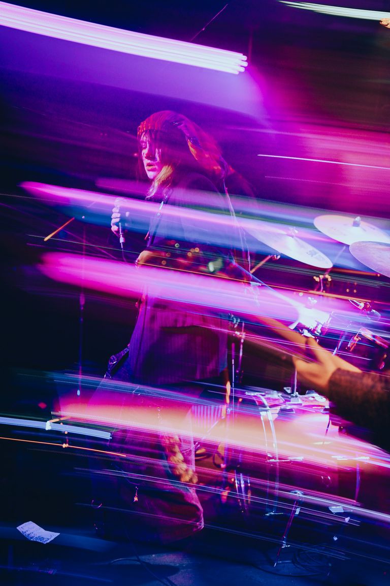 Live musical performance captured with vibrant pink light trails and long exposure motion blur on a dark stage during a concert event.